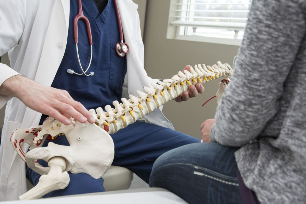 Chiropractor holding fake spine explaining Spinal Stenosis to patient